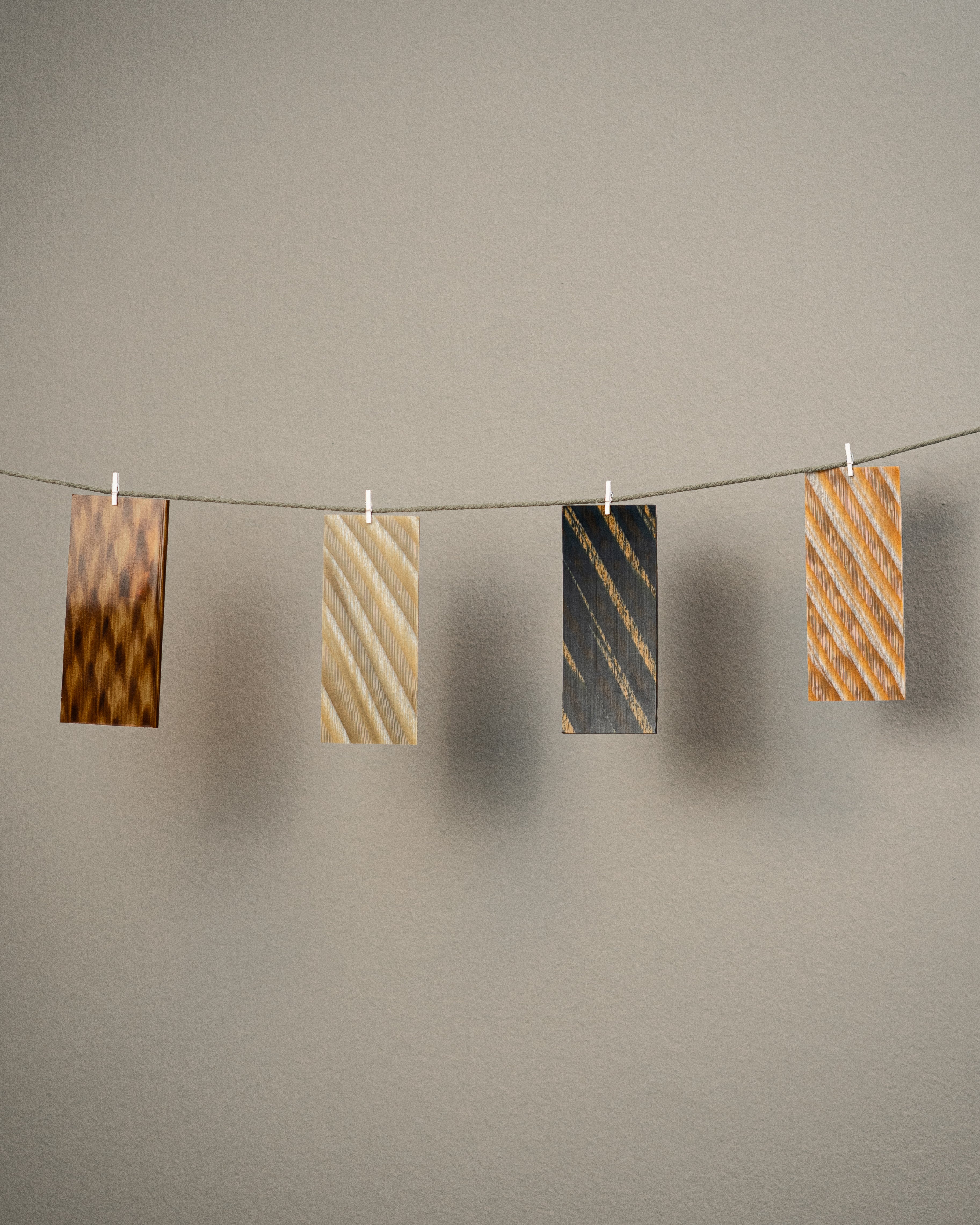 Four textured cards in earth tones hanging with mini clothespins on a string against a gray wall.